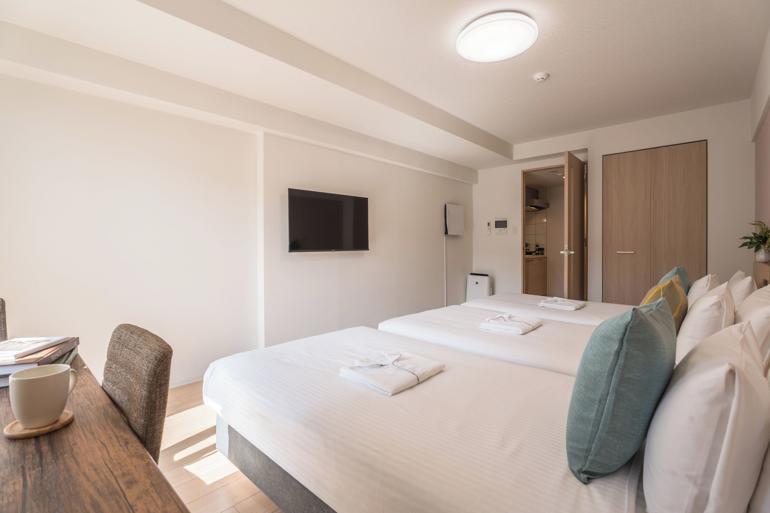 A hotel room with two beds, a TV, a desk with a chair, and a wardrobe.