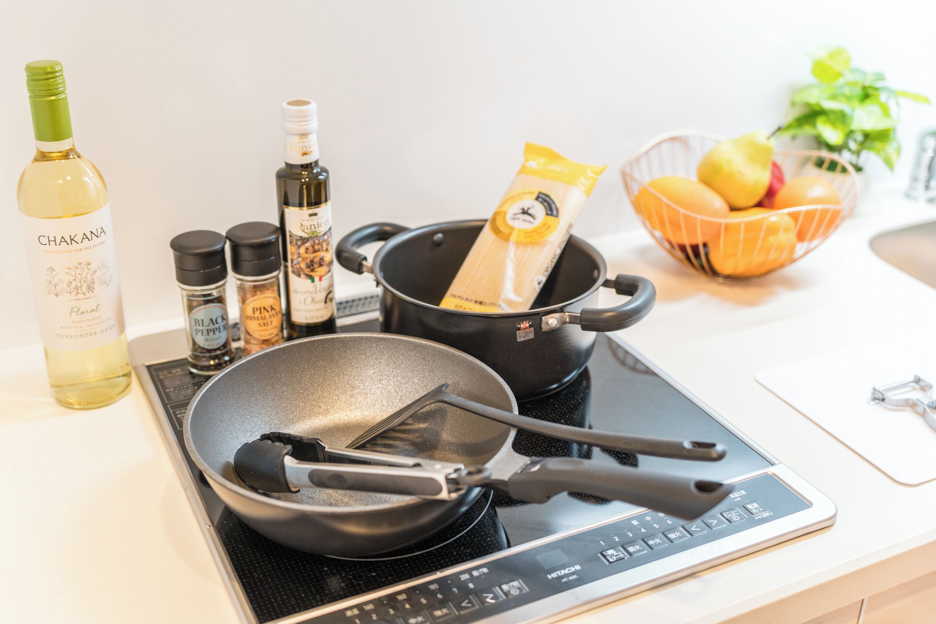Une cuisine équipée d’une poêle, d’ustensiles de cuisine, d’une bouteille de vin Chakan et d’un saladier rempli de fruits.