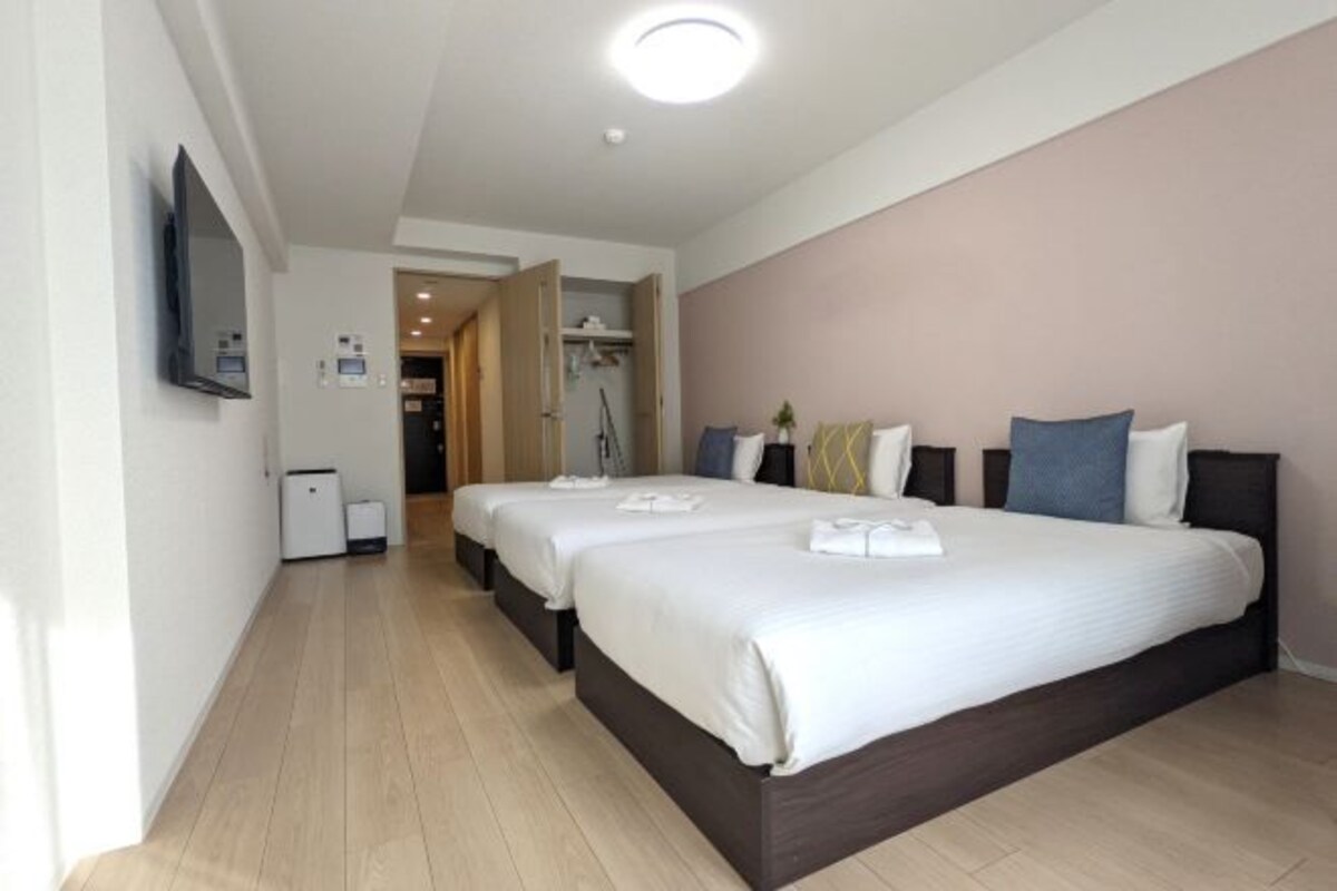 Quarto de hotel com duas camas, televisão, espelho e área de chuveiro.