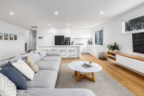 Relax in a spacious living area with a sofa and coffee table, leading to a sleek kitchen with white cabinetry and a refrigerator.