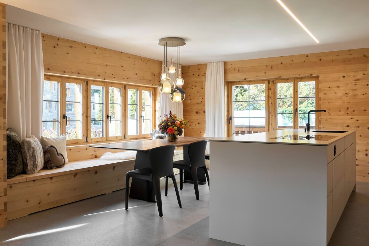 Una cocina moderna con paredes de madera, una isla central y un área de estar junto a las ventanas.