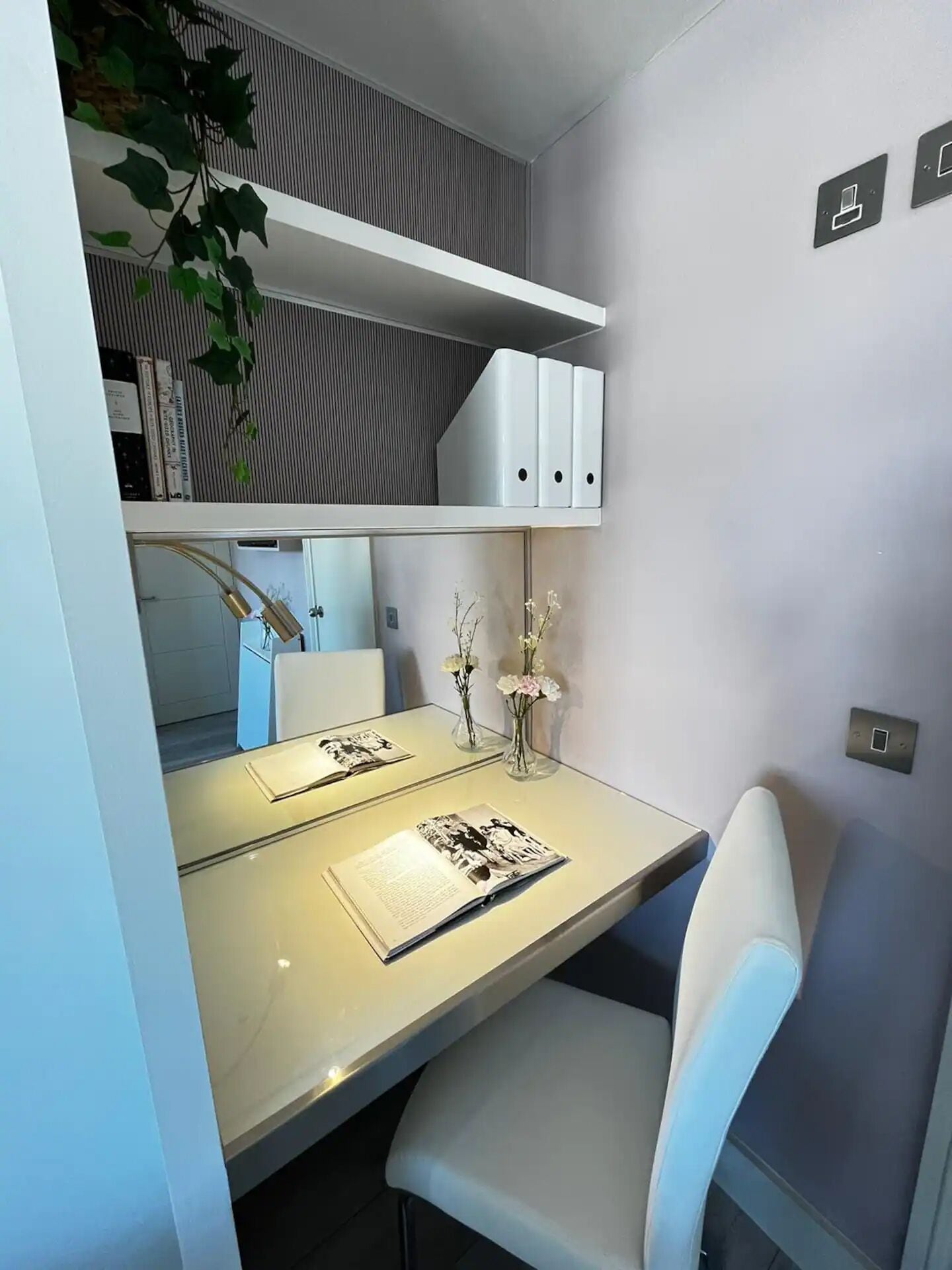 Un espace de bureau moderne avec un bureau blanc, une chaise, une étagère contenant des classeurs et une plante.