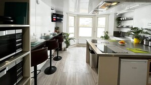 A modern kitchen with a central island, bar stools, a Bosch dishwasher, and a flat-screen TV mounted above the island. - Apt. 12 - Luxury Living Chic Studio Steps from Beach (Brighton and Hove)