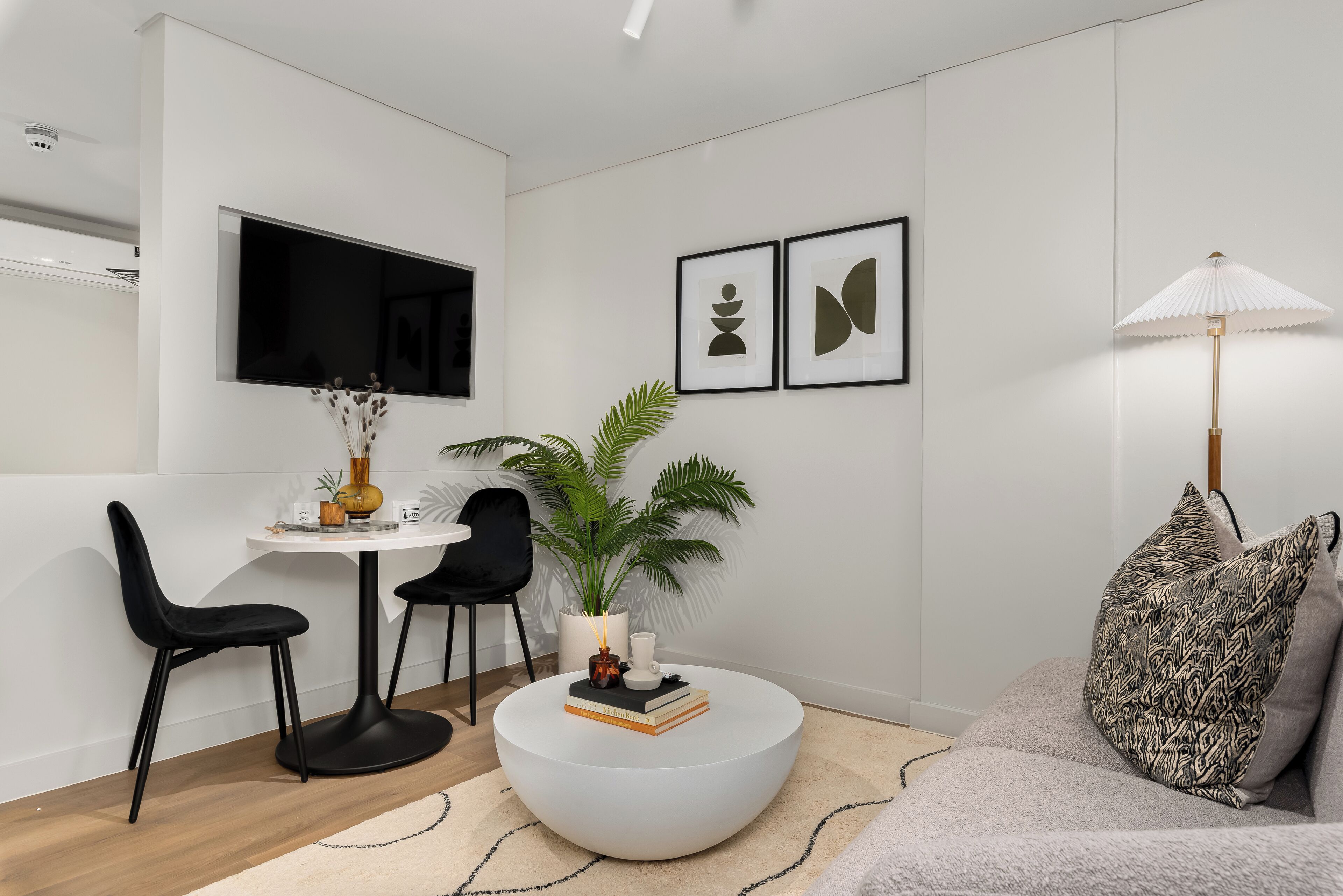 A modern living room with a round white coffee table, black chairs, a sofa, a TV mounted on the wall, and framed artwork.