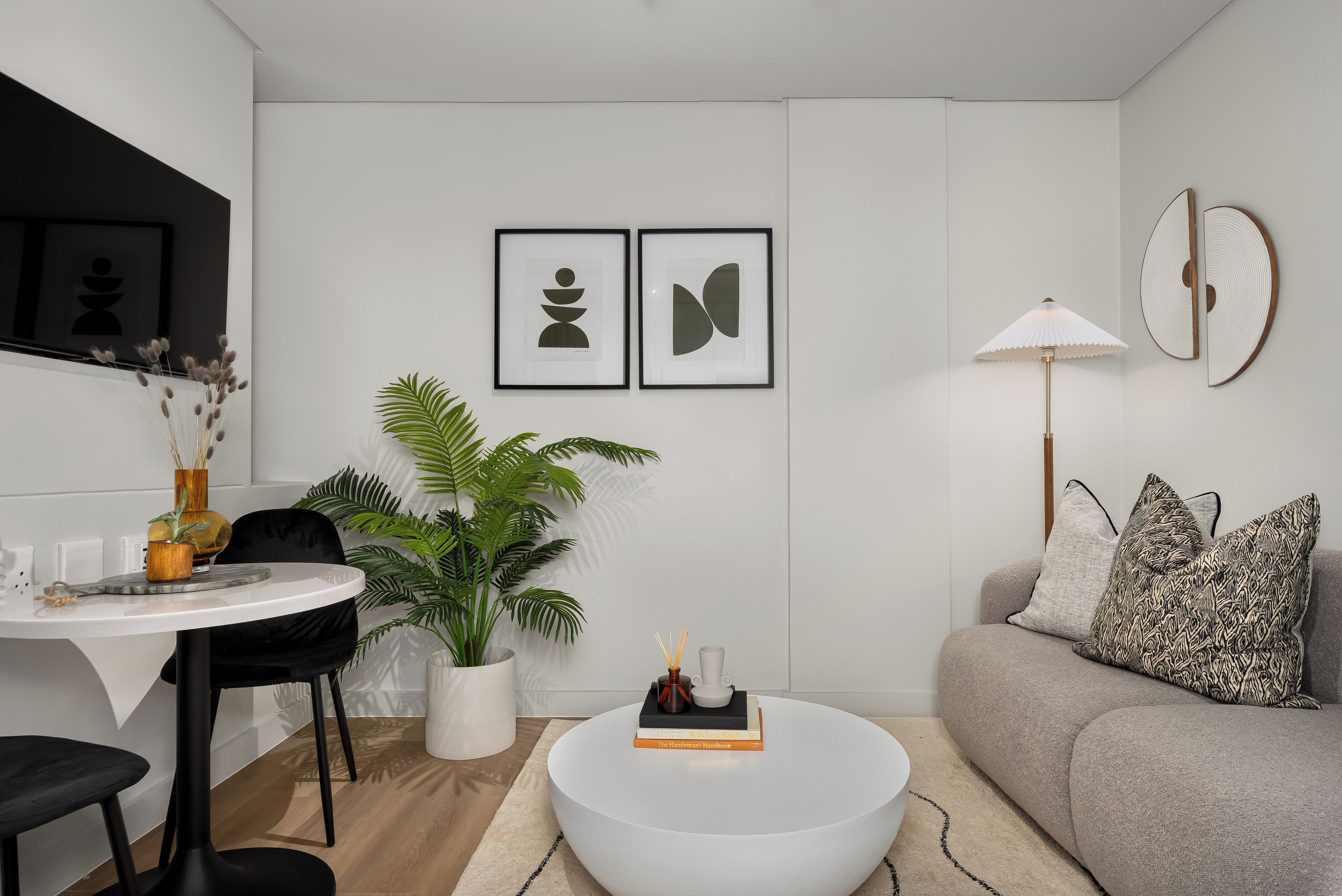 Una sala de estar moderna con una mesa de centro redonda, un sofá, una mesa de comedor con sillas y una planta en maceta.