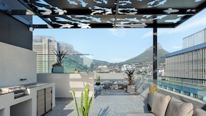 A rooftop terrace with a modern outdoor kitchen, seating area, and potted plants. - The Tokyo 003 (Cape Town)