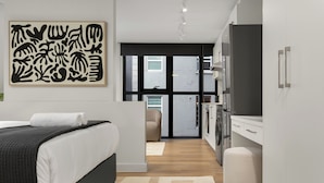 A modern bedroom with a bed, a large abstract painting, a wardrobe, and a view through a glass door to a balcony. - The Tokyo 003 (Cape Town)