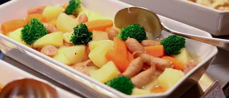 A buffet with various dishes including potatoes, carrots, broccoli, and sausages.