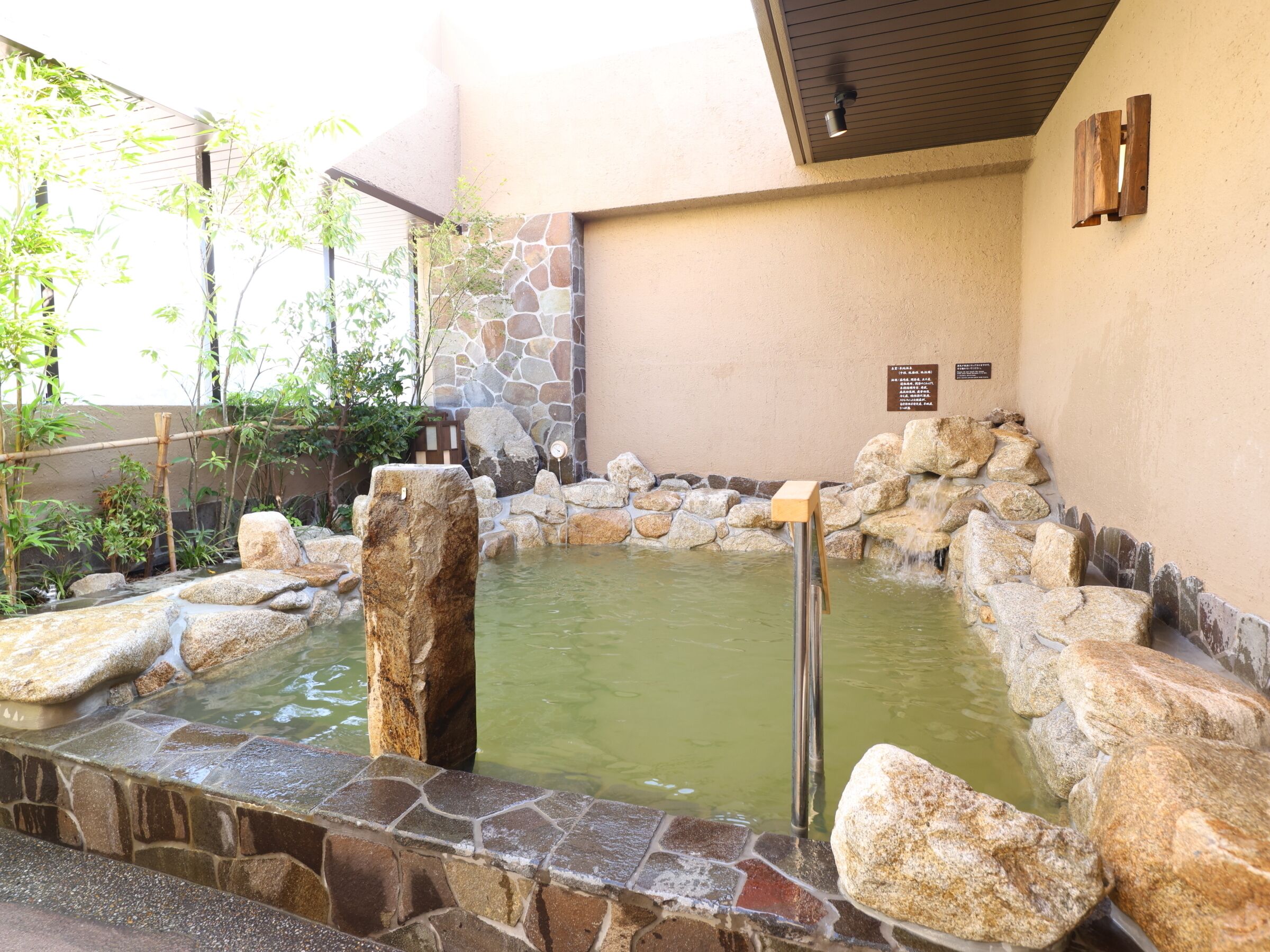 Un espace de détente aménagé avec de la pierre et du bois, comprenant une petite piscine, le tout entouré de rochers et de plantes.