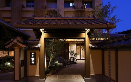 A traditional Japanese building entrance with a tiled roof, stone pathway, and a sign with Japanese characters.