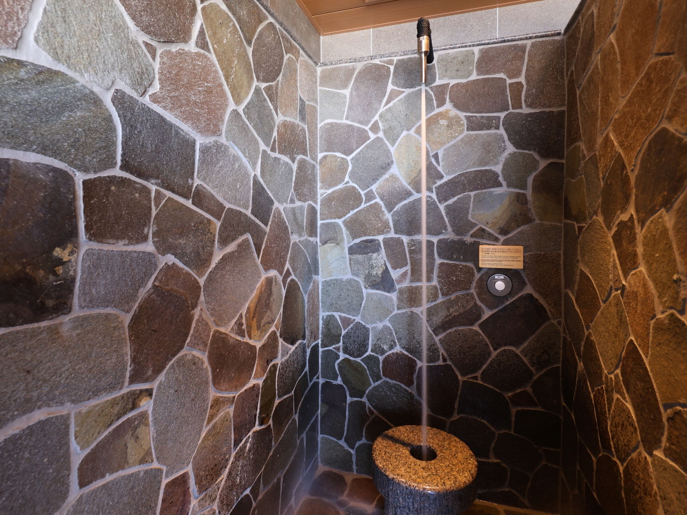Ducha con paredes de piedra, un lavabo de piedra y un cabezal de ducha.