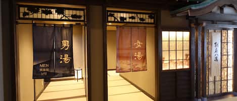 A traditional Japanese interior with tatami mat flooring, sliding doors, and signage indicating separate areas for men and women.