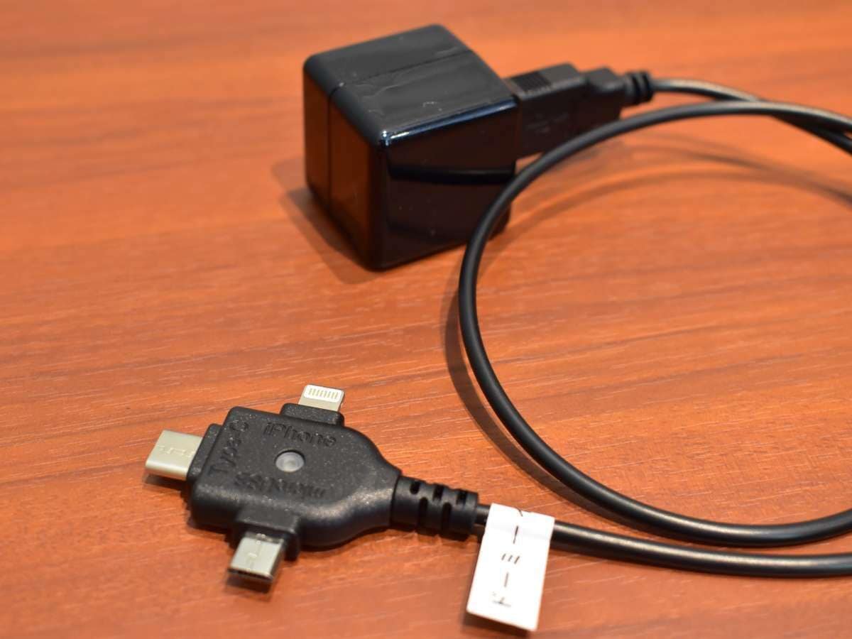 Adaptador de tomada preto com cabo USB sobre uma superfície de madeira.