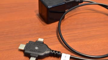 En svart strömadapter med en USB-kabel, placerad på en träyta.