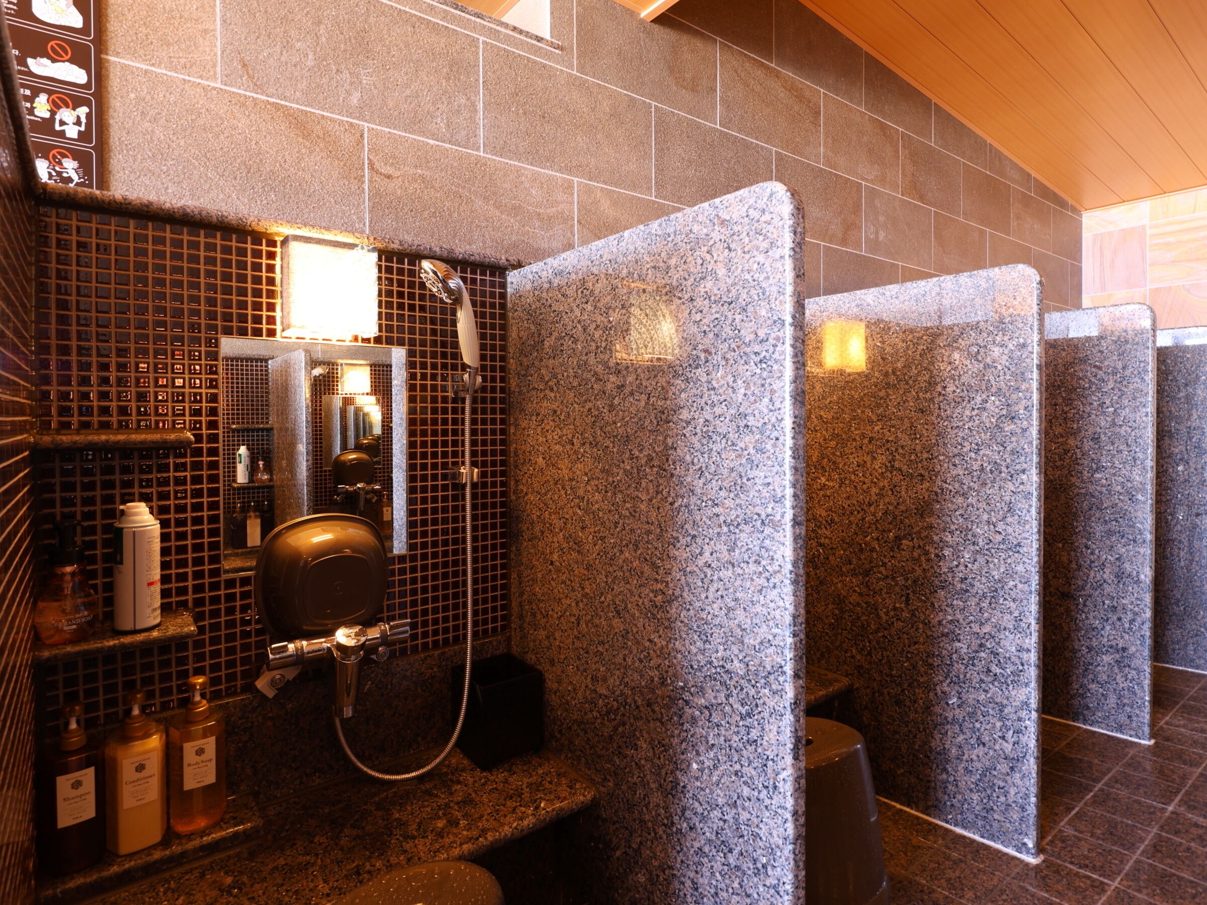 A public restroom with granite walls, a hand dryer, and a mirror.