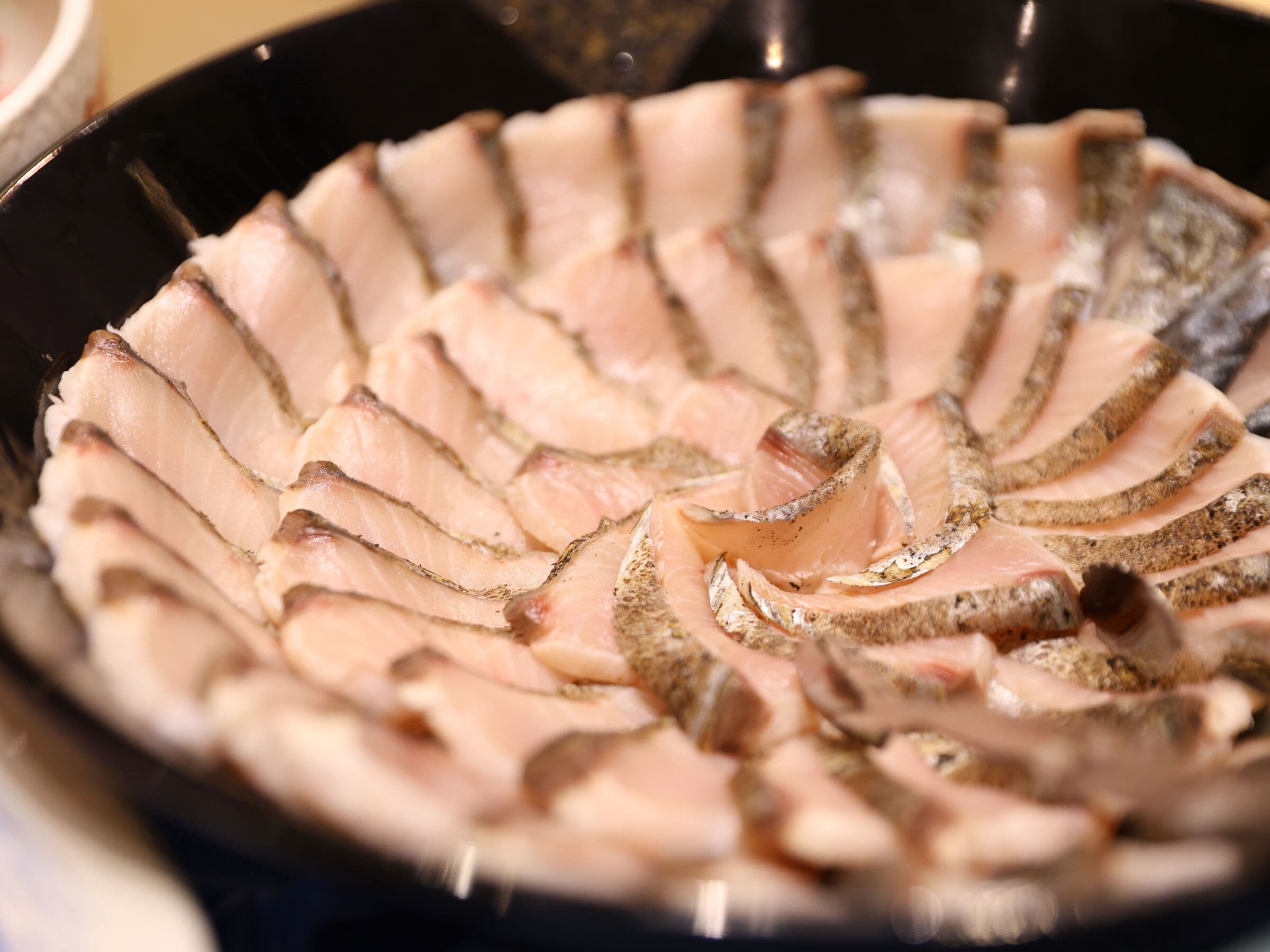 A close-up of sliced fish arranged in a circular pattern on a pan.