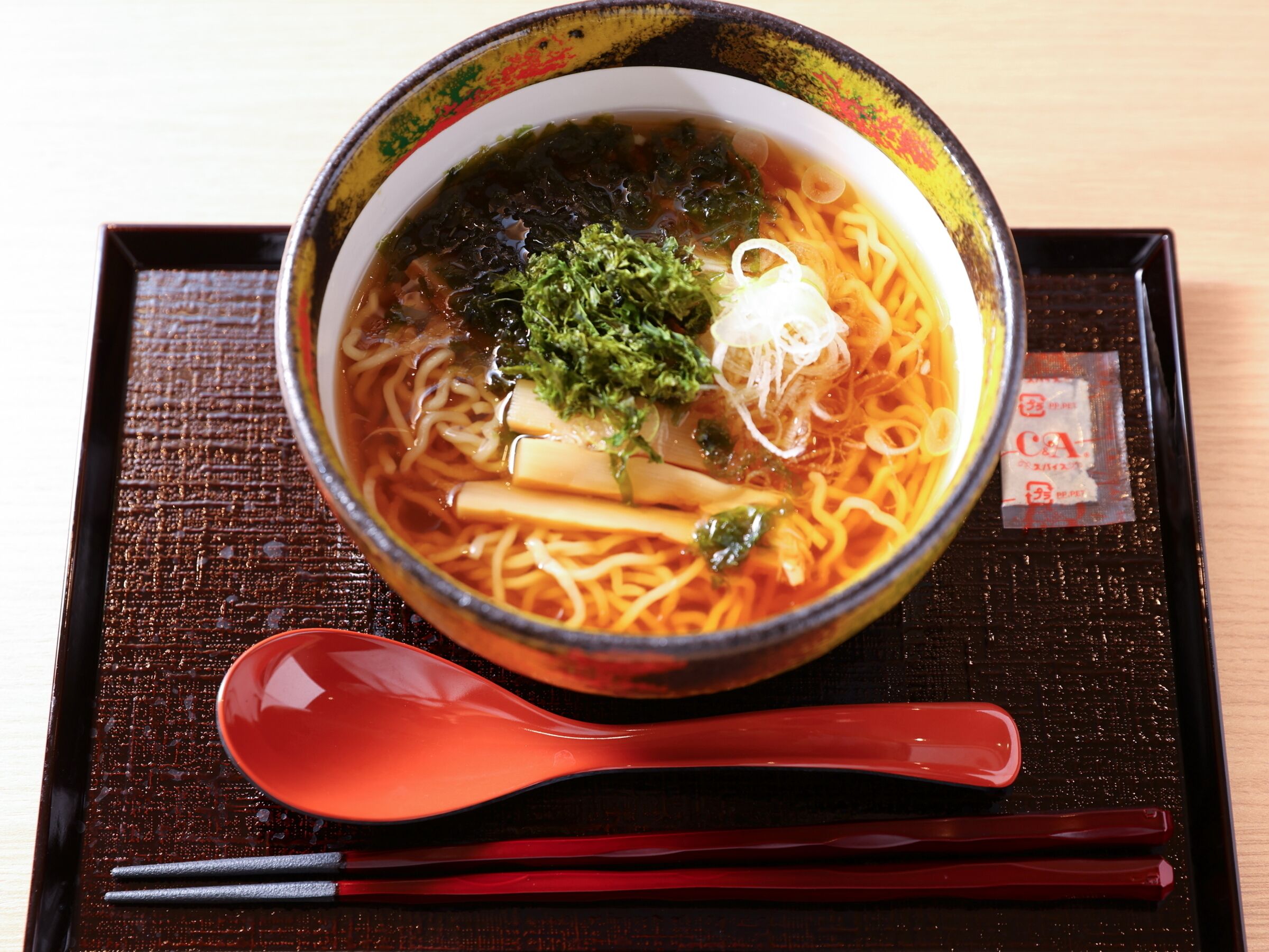 A bowl of ramen with noodles, broth, and toppings on a tray with chopsticks and a spoon.