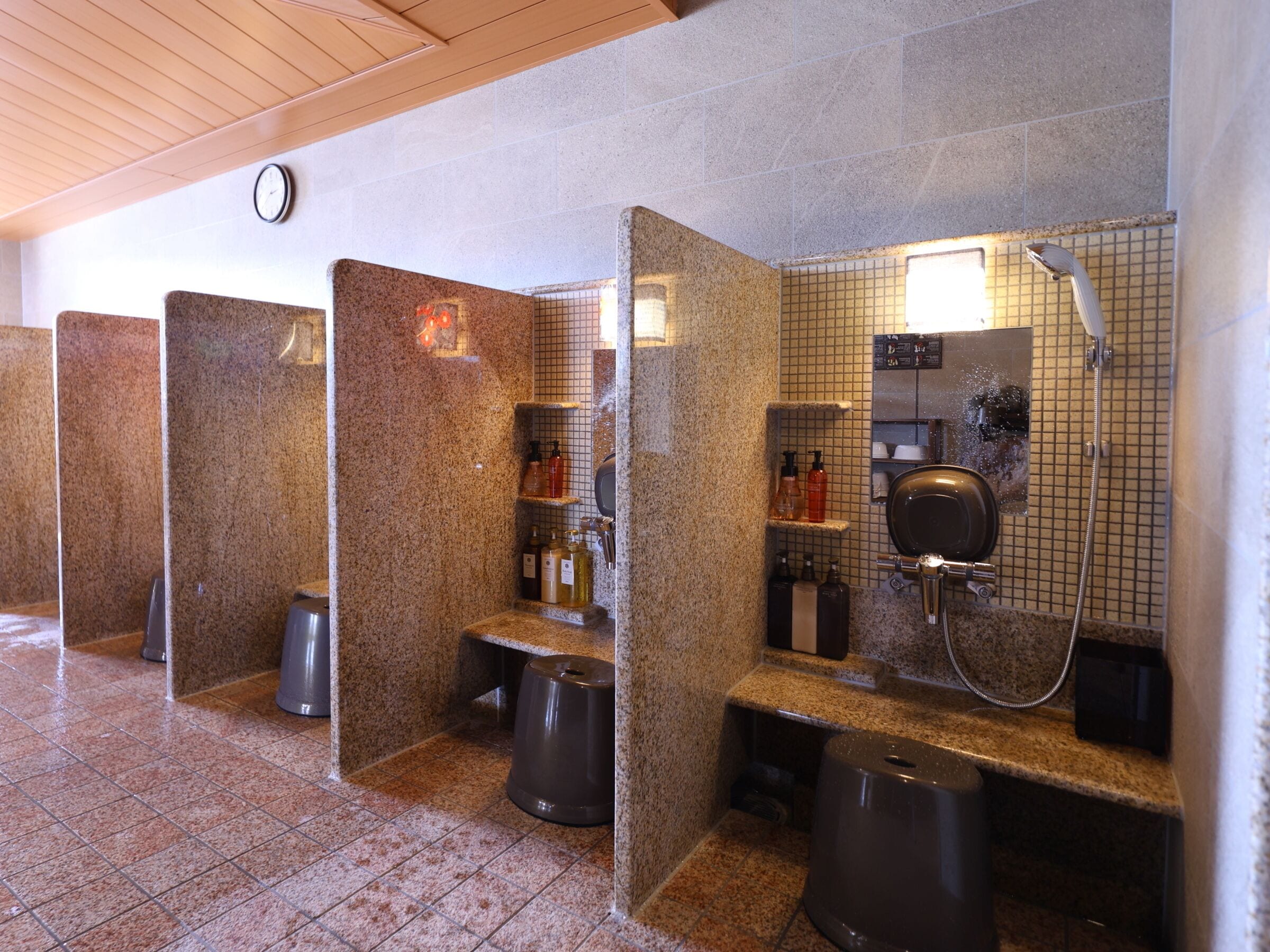 Un bagno pubblico con divisori in granito, un orologio e una parete piastrellata con area docce.