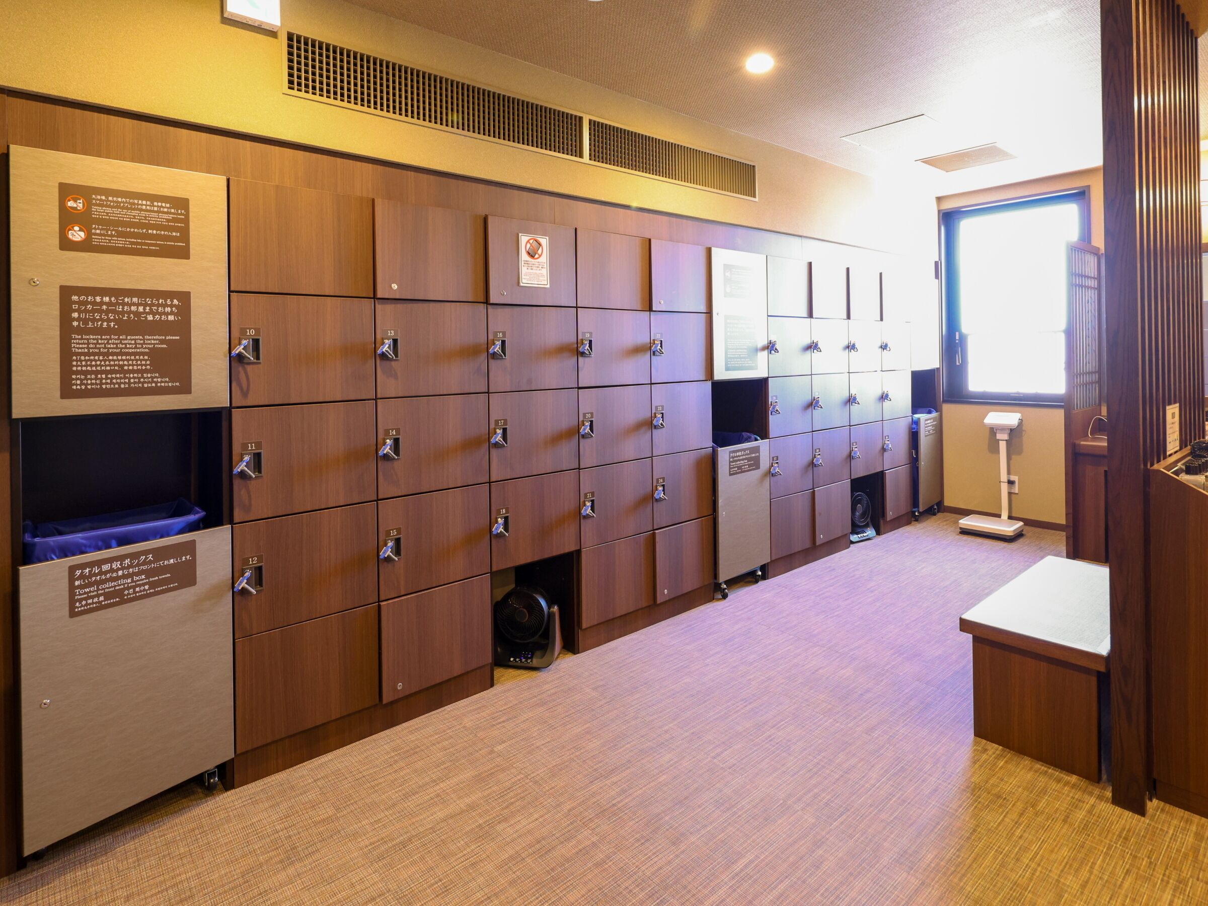 A row of wooden lockers with numbered tags, a towel collection box, and a scale.