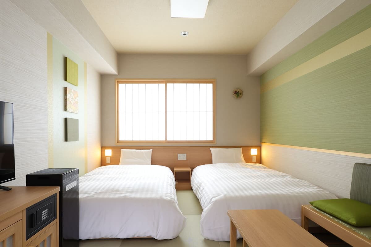 Een hotelkamer met twee bedden, een televisie, een minibar en een raam met zonwering.