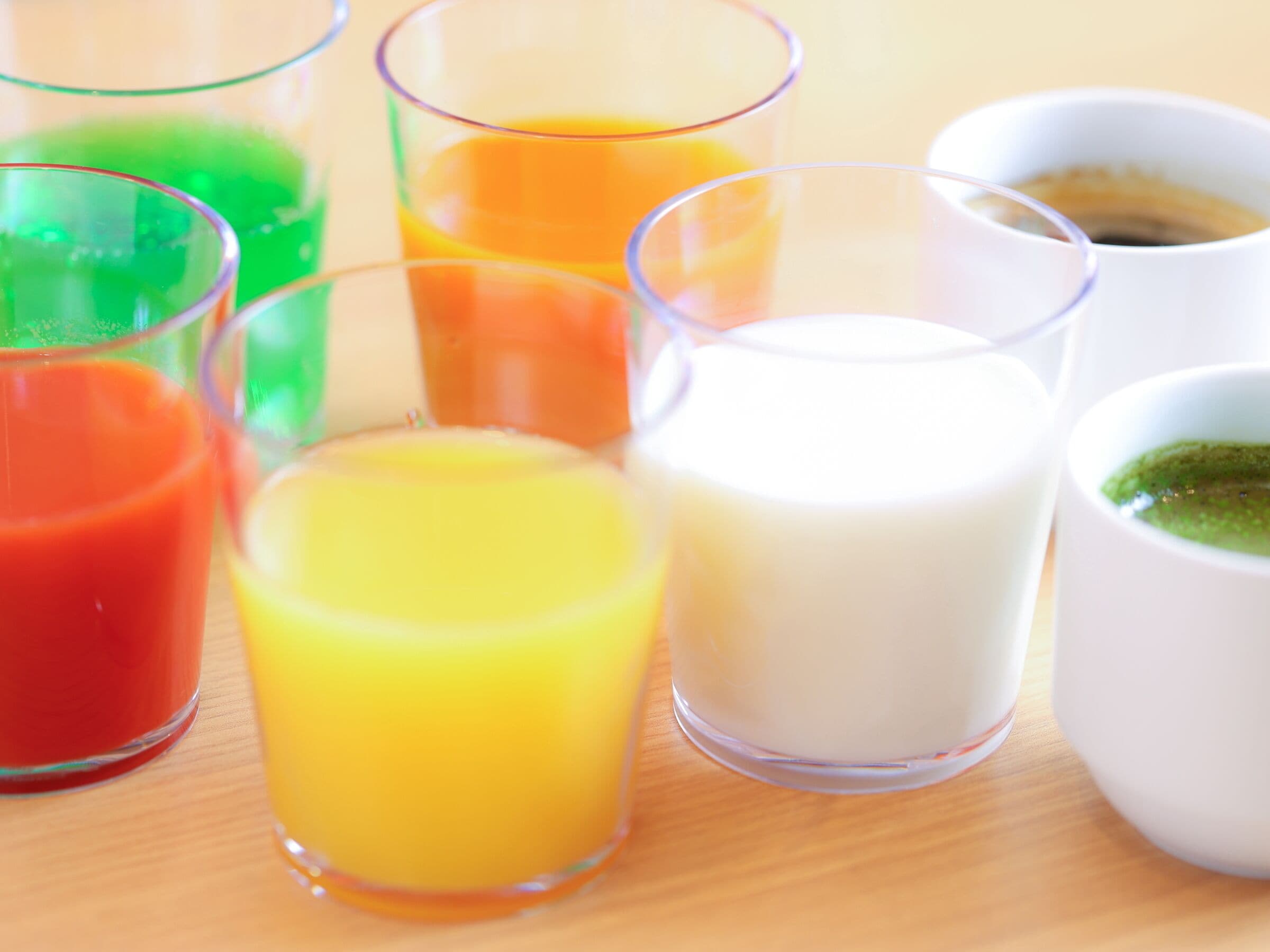 On peut voir une variété de récipients en verre transparent contenant différents liquides colorés, qui pourraient être des jus de fruits ou d’autres boissons, posés sur une surface en bois.
