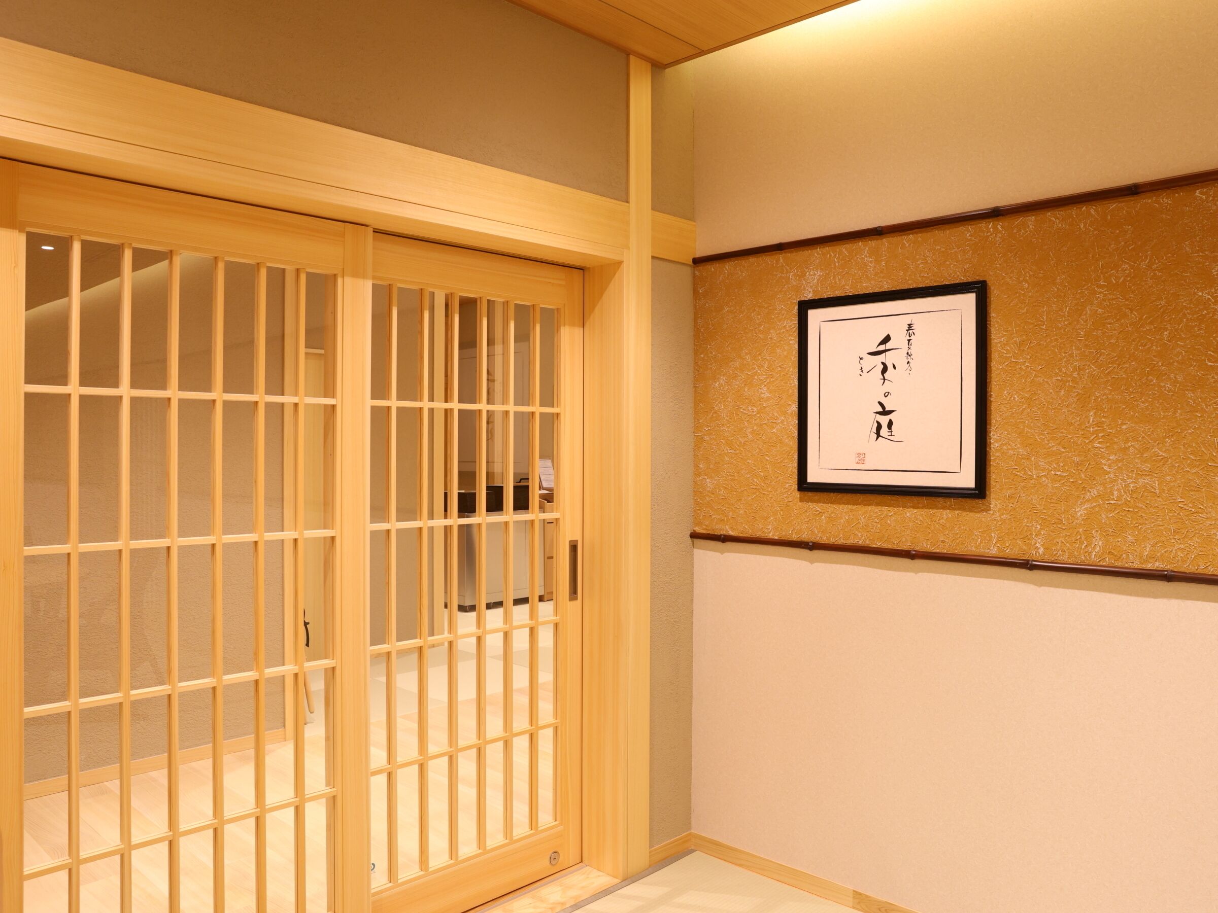 A room with a sliding wooden door, a framed calligraphy piece on the wall, and a carpeted floor.