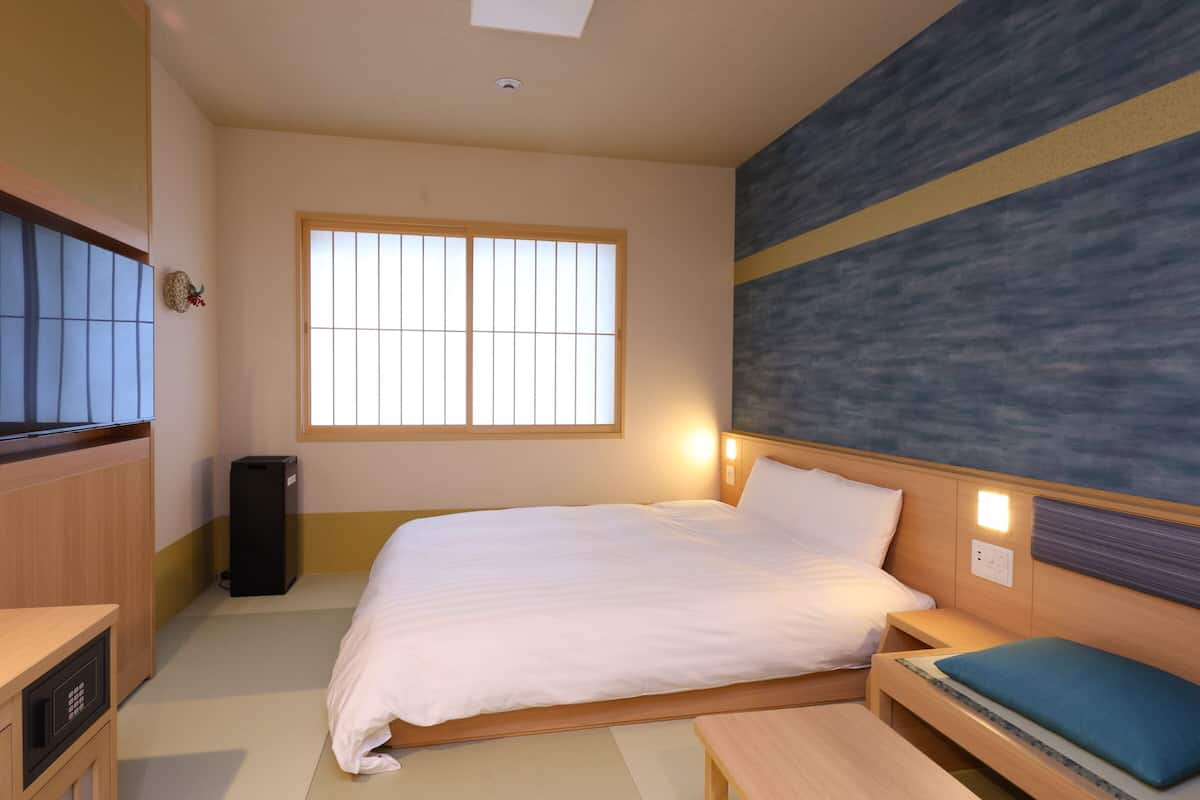 Een hotelkamer met een bed, nachtkastje en een groot raam.