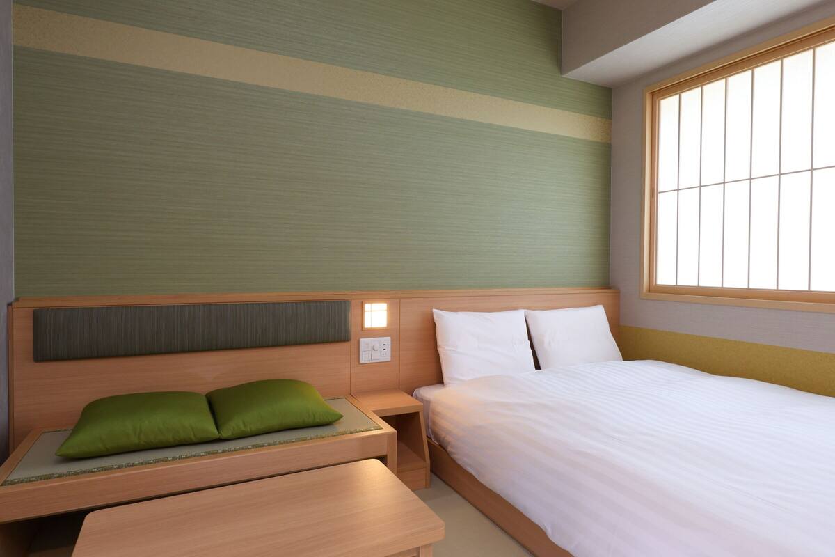 Een hotelkamer met een bed, nachtkastje en een klein bureau met stoel.
