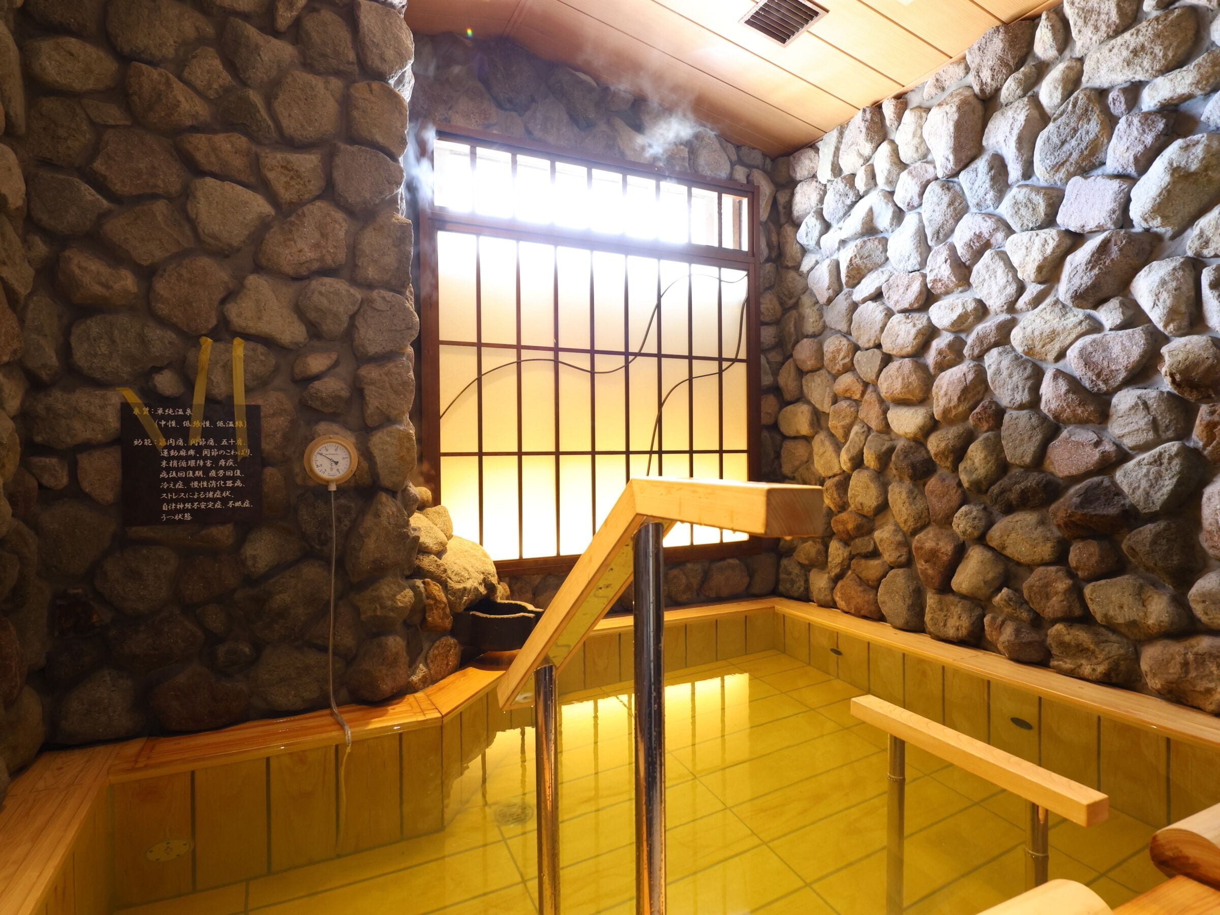 Un onsen japonés tradicional con paredes de piedra, un banco de madera y suelo de baldosas.