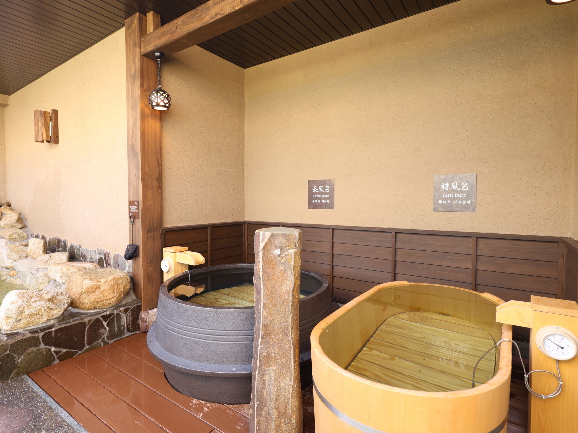 A traditional Japanese onsen with stone and wooden baths, wooden benches, and a wooden ceiling.