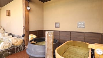 A traditional Japanese onsen with stone and wooden baths, wooden benches, and a wooden ceiling.