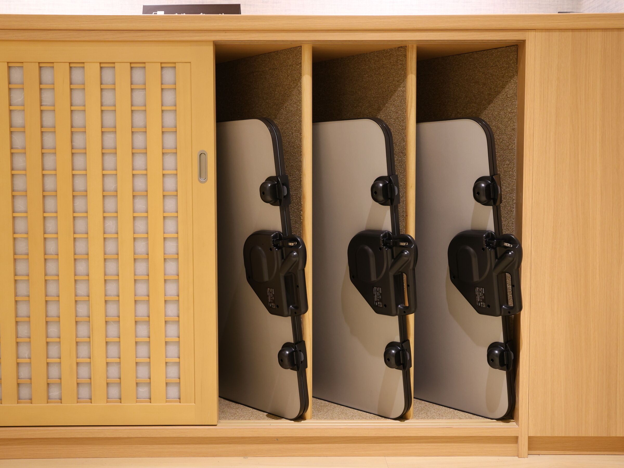 A wooden cabinet with a grid-patterned door and two compartments containing black objects.