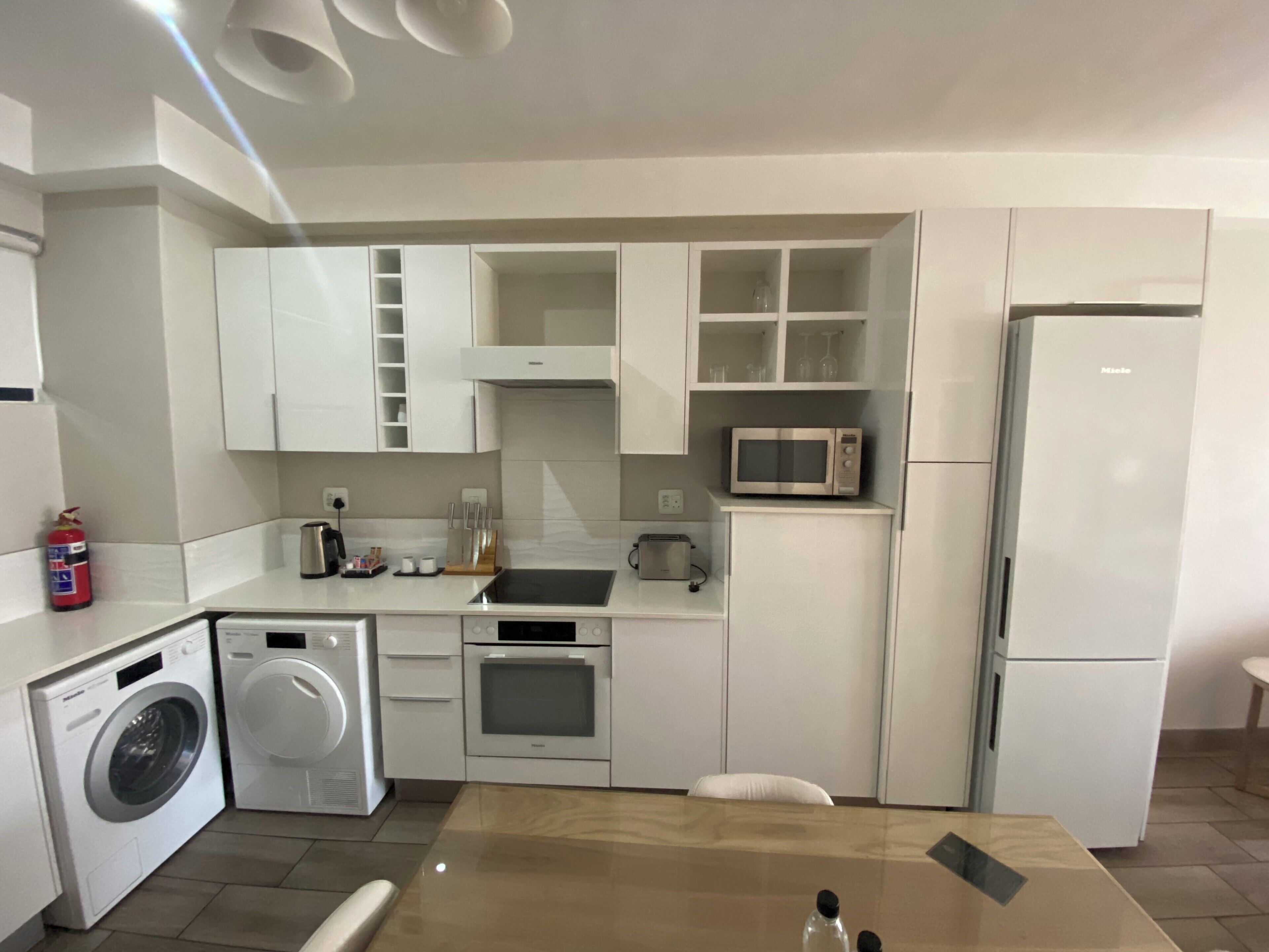 Une cuisine compacte avec des meubles blancs, un four à micro-ondes, un grille-pain et un lave-linge.