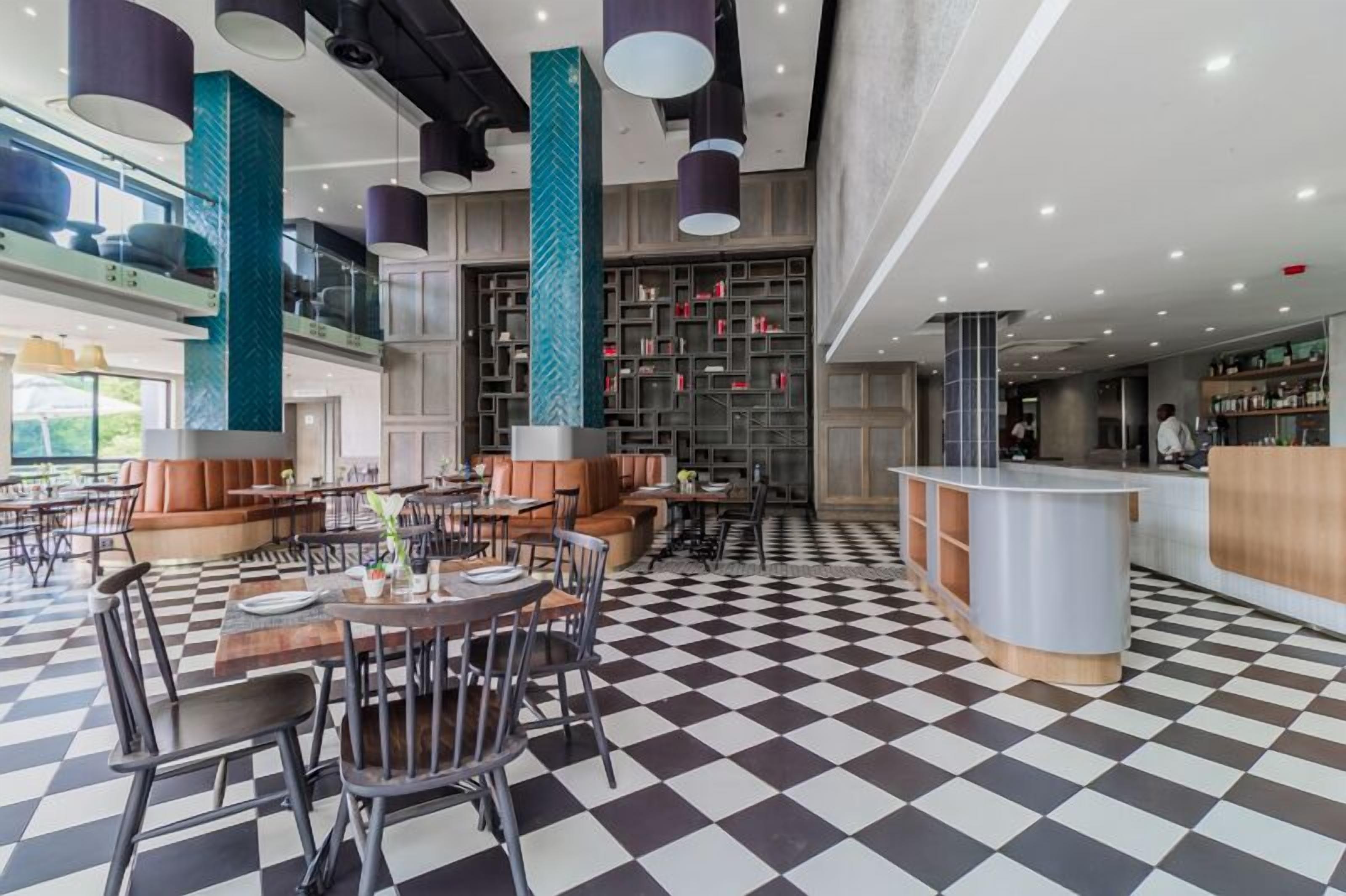 A modern restaurant with checkered flooring, high ceilings, and a central seating area with tables and chairs.