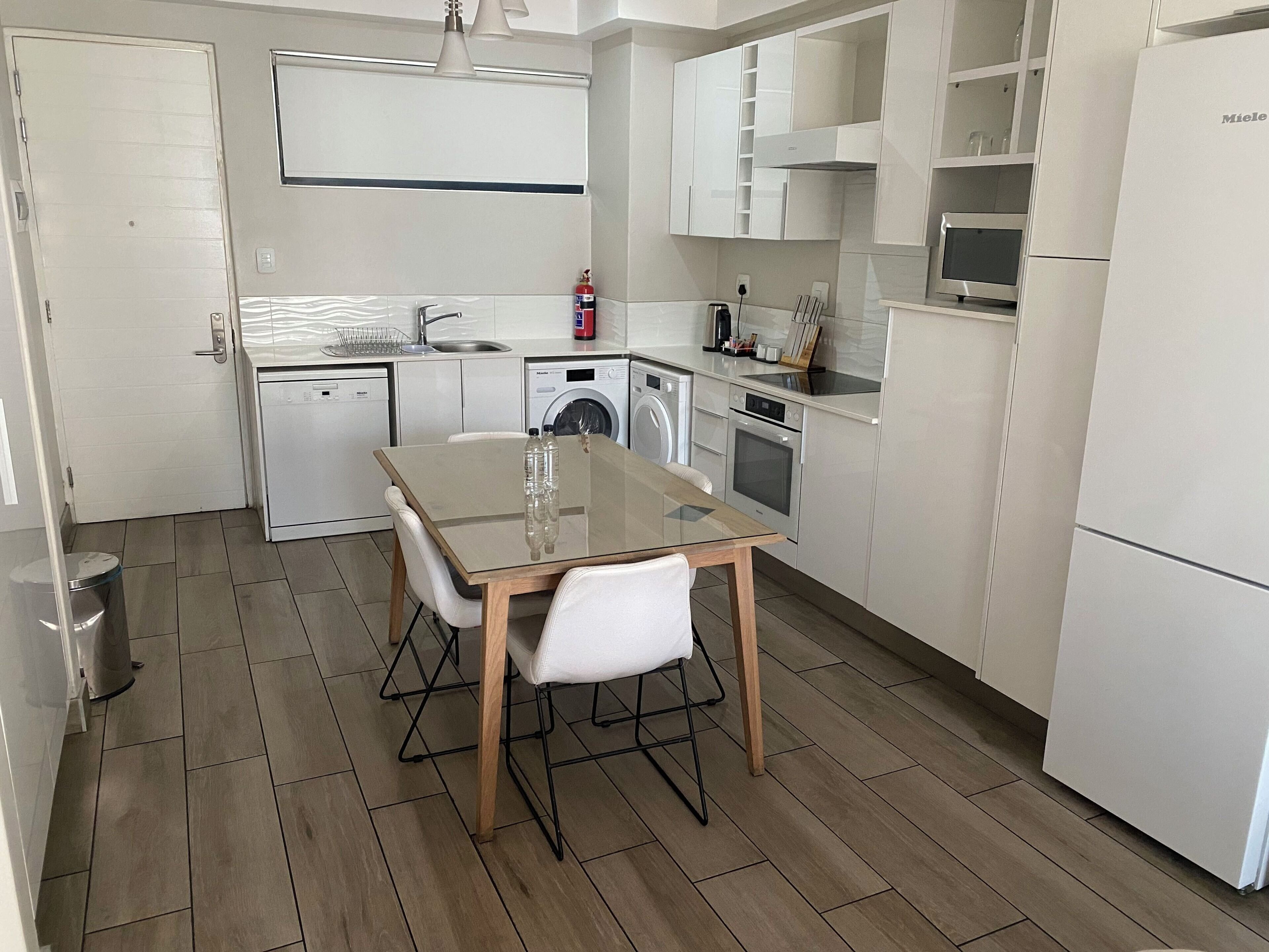A modern kitchen with white cabinetry, a glass-top dining table, and a washing machine.