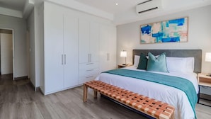Un dormitorio moderno con una cama grande, un banco, un armario y un cuadro en la pared.