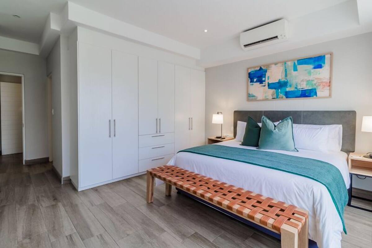 Un dormitorio moderno con una cama grande, un banco, un armario y un cuadro en la pared.