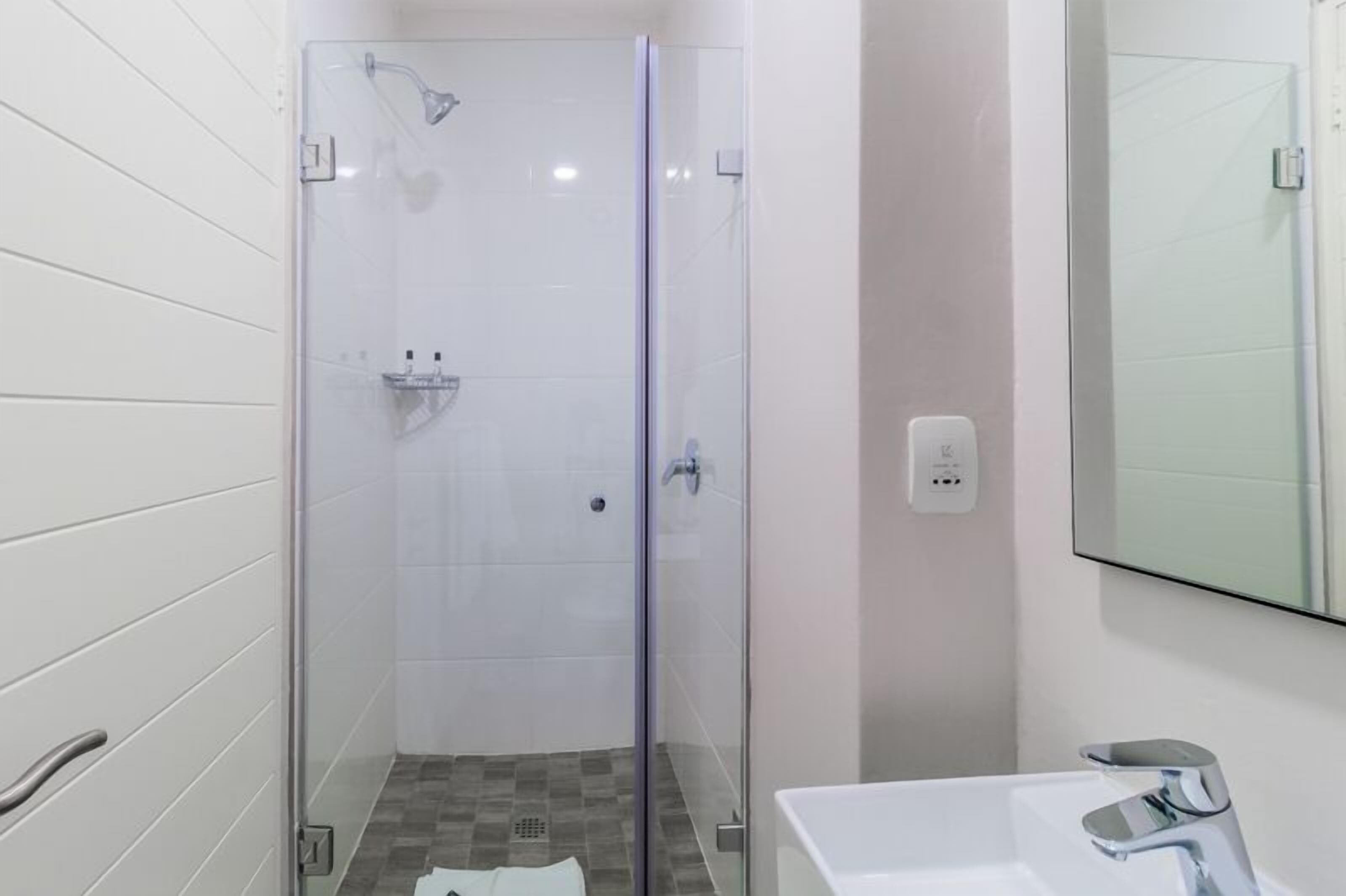 Une salle de bain moderne avec une douche à parois de verre, un lavabo blanc et un miroir.