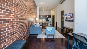A modern living room with a brick wall, a ceiling fan, a dining area, and a kitchen in the background. - Rose at the Millennium - Stylish 1 BR in Houston (Houston)