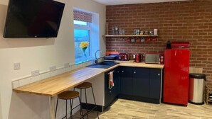 Een moderne keuken met een houten aanrecht, twee barkrukken, een rode koelkast en een aan de muur bevestigde televisie.