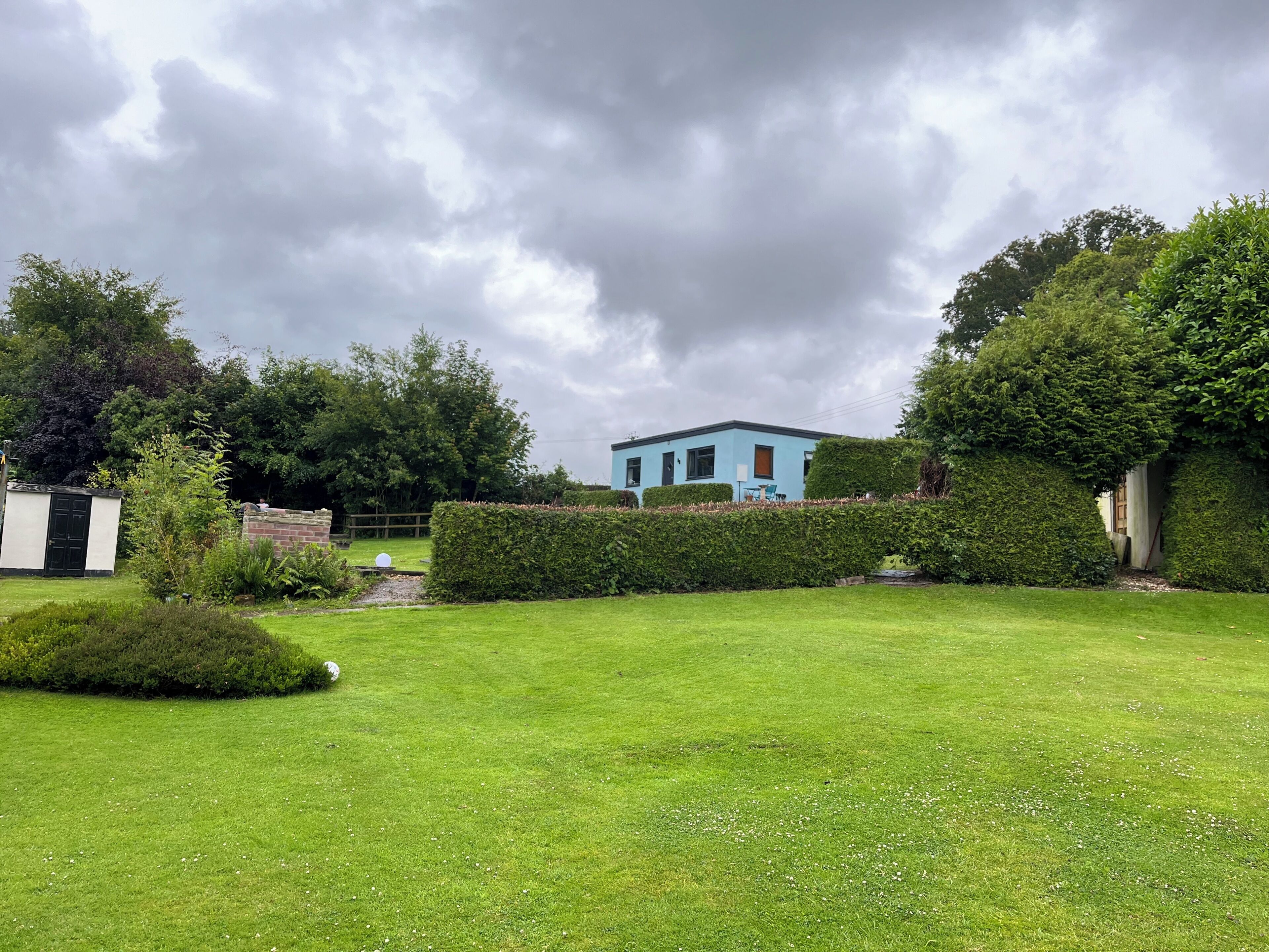 A residential property with a well-maintained lawn, a blue house, and a hedge.