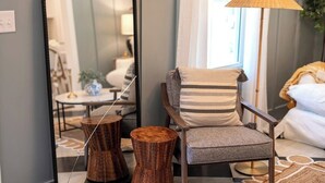 Une chambre moderne avec un mur miroir, une chaise en bois avec un coussin à rayures, un lampadaire et un lit avec une literie blanche.