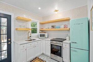 A compact kitchen with white cabinets, a stove, a microwave, and a teal refrigerator.