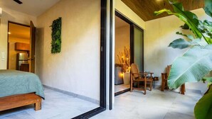 A modern hotel room with a bed, a seating area with chairs, a large plant, and a view through a glass door. - MICAELA apartment, pool, AC next to the lagoon (Bárbara Guerrero Pérez)