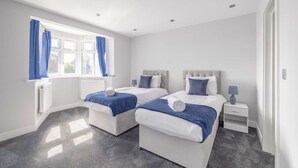 Een moderne hotelkamer met twee bedden, een raam met blauwe gordijnen, een witte nachtkastje en een grijze vloerbedekking.