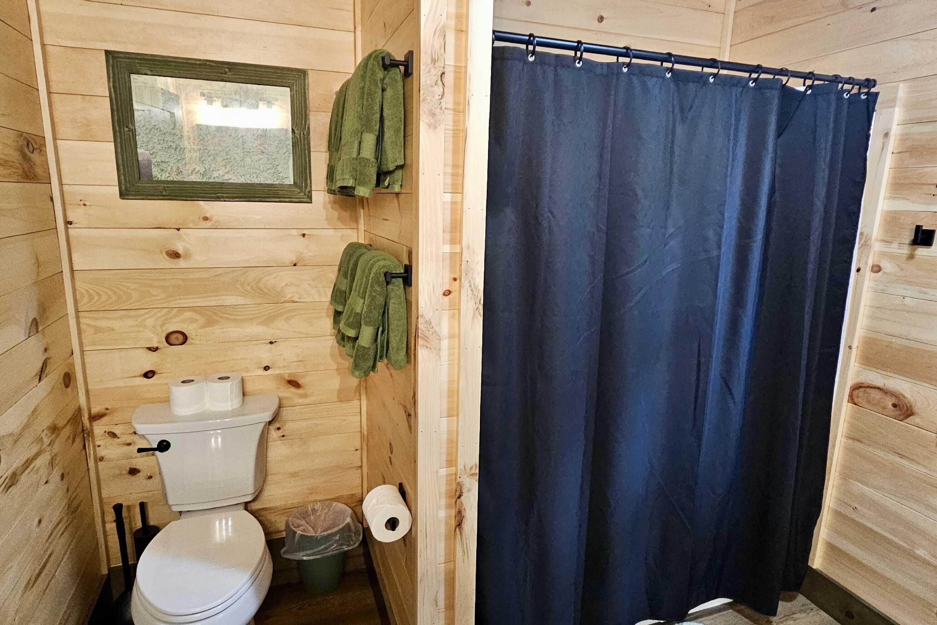 A wooden cabin bathroom with a toilet, two rolls of toilet paper, a green towel, and a blue shower curtain.