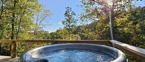 Un jacuzzi en una terraza de madera con vista al bosque.