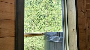 Una cabaña de madera con un ventanal grande que da a un  área boscosa y un risco rocoso.