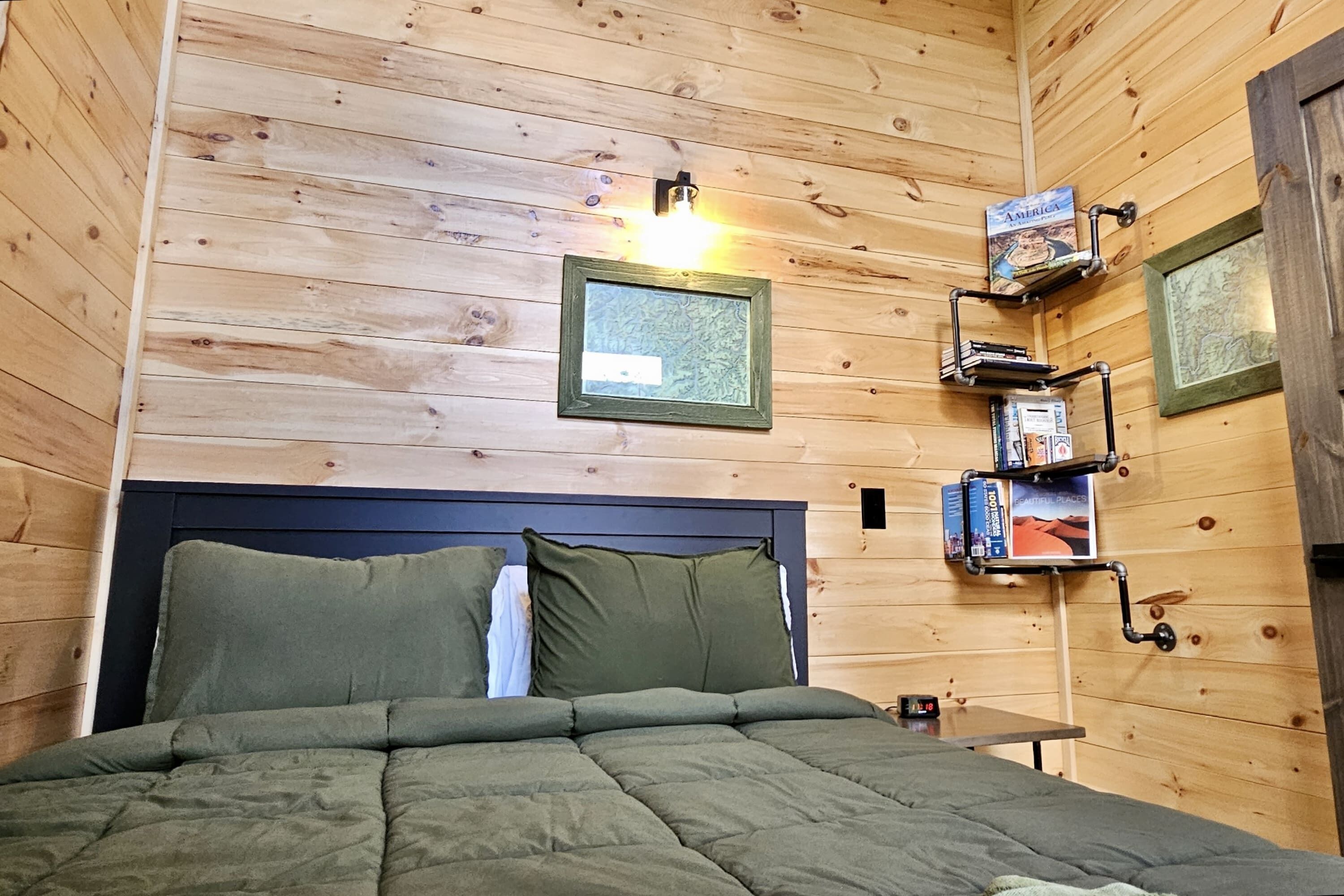 A wooden-paneled room with a bed, a wall-mounted shelf with books, and a framed picture.