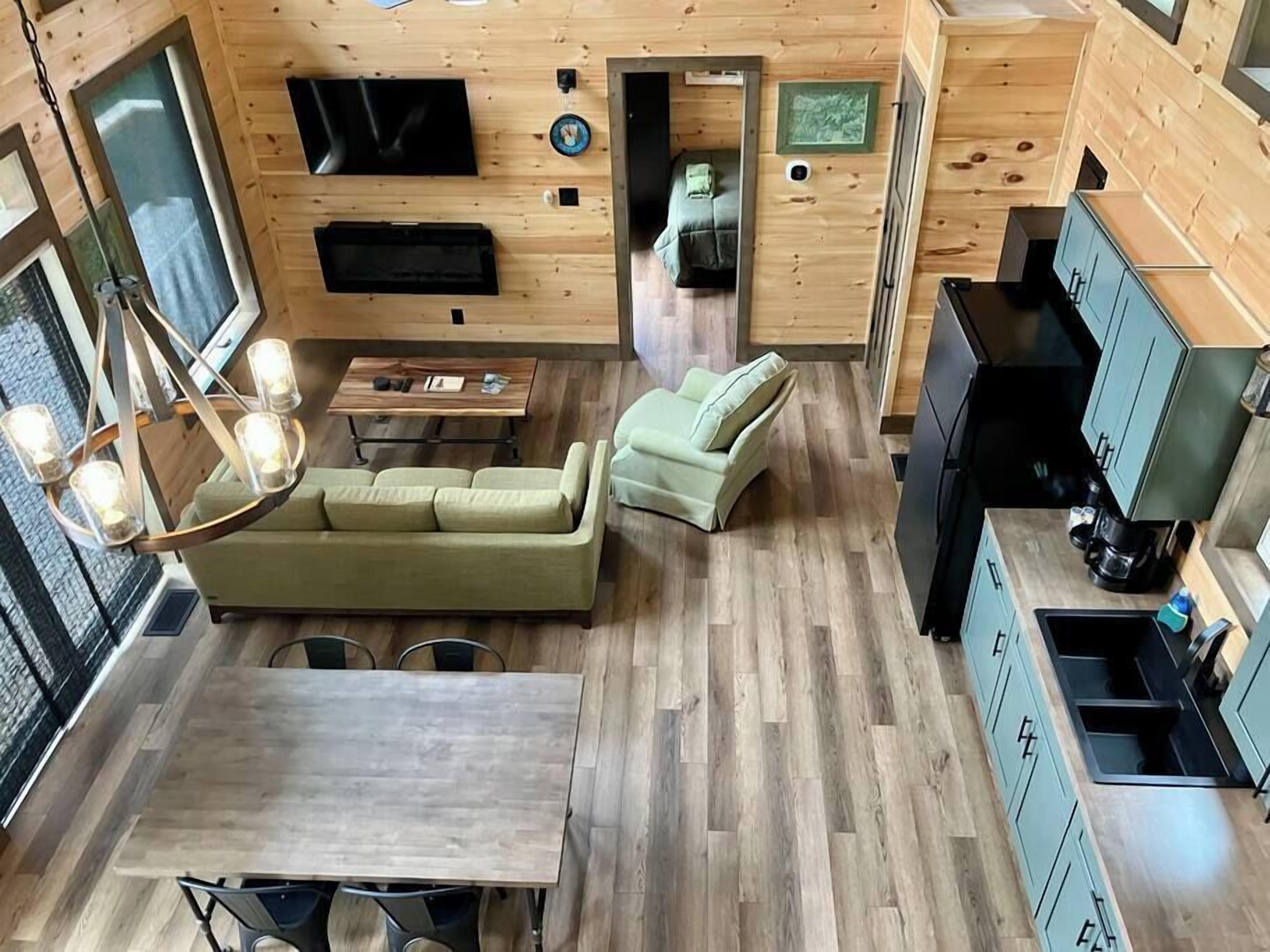 A compact, modern cabin with a wooden interior, a dining area, a sofa, a TV, and a kitchenette.
